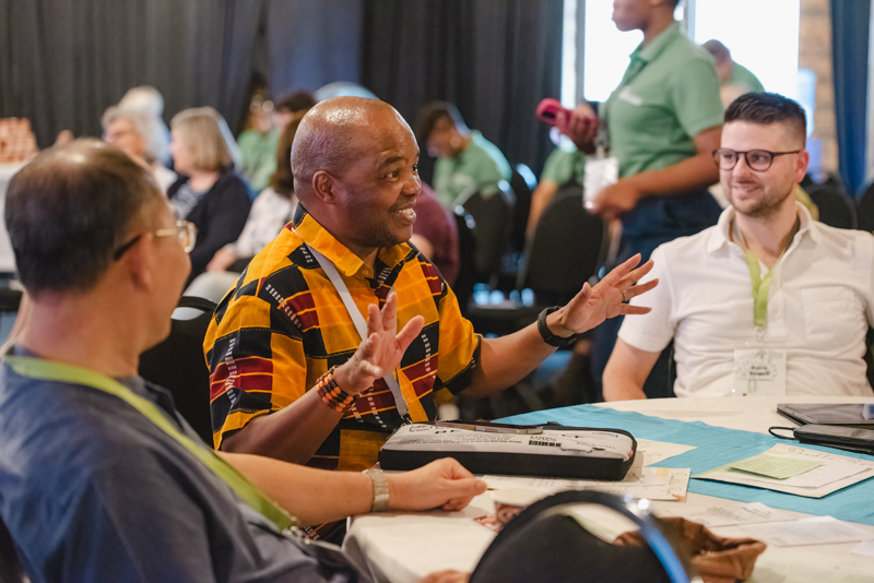 Tablegroup discussions took place throughout the Global Gathering. Here we see a representative in a bright yellow shirt, talking with two other participants.