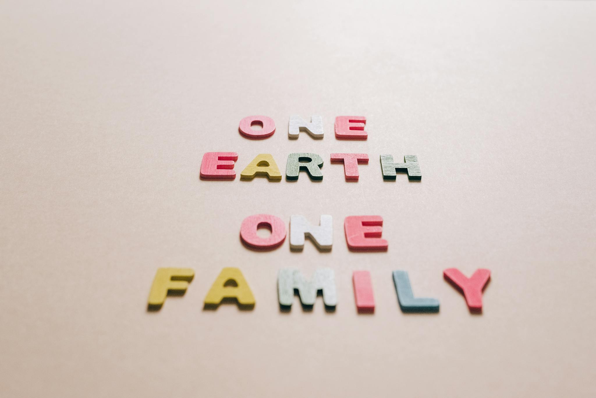 Multicolored letters spelling 'One Earth One Family' on a beige backdrop, promoting unity.